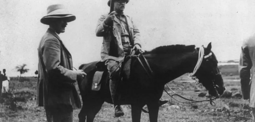 Theodore Roosevelt sitting astride a horse and holding a musket.