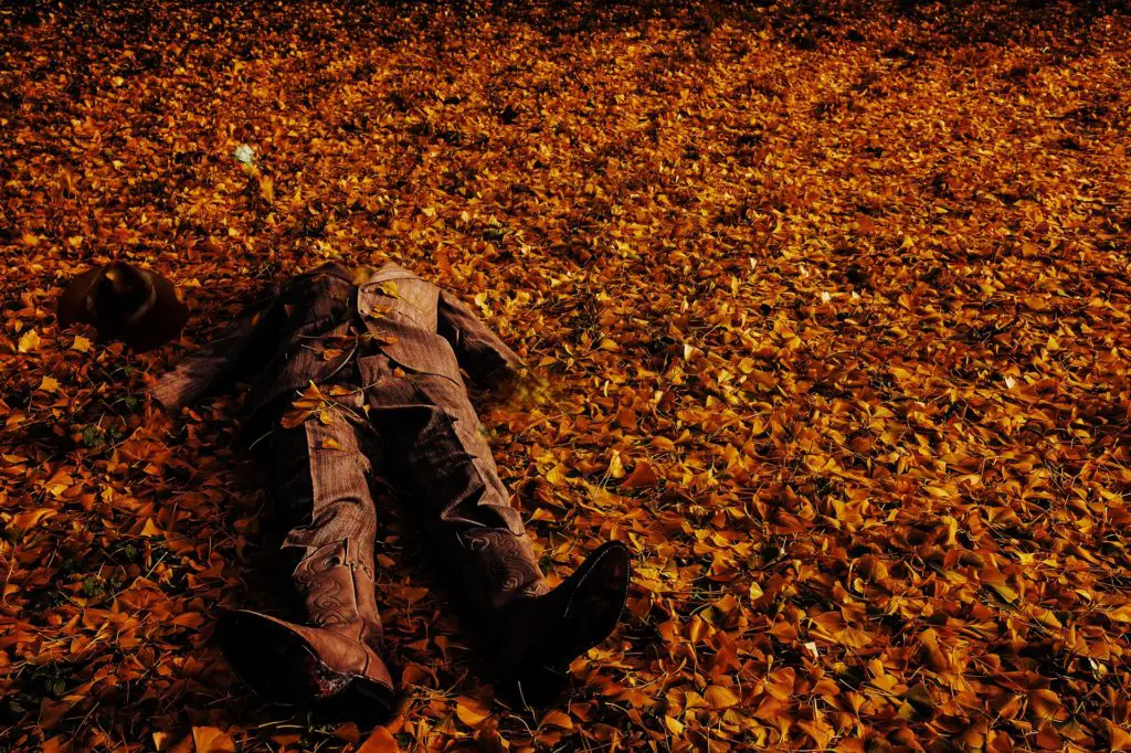 A mockup of a man's body in a suit on the ground with leaves scattered everywhere.