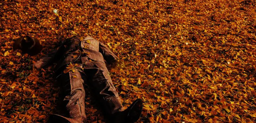 A mockup of a man's body in a suit on the ground with leaves scattered everywhere.