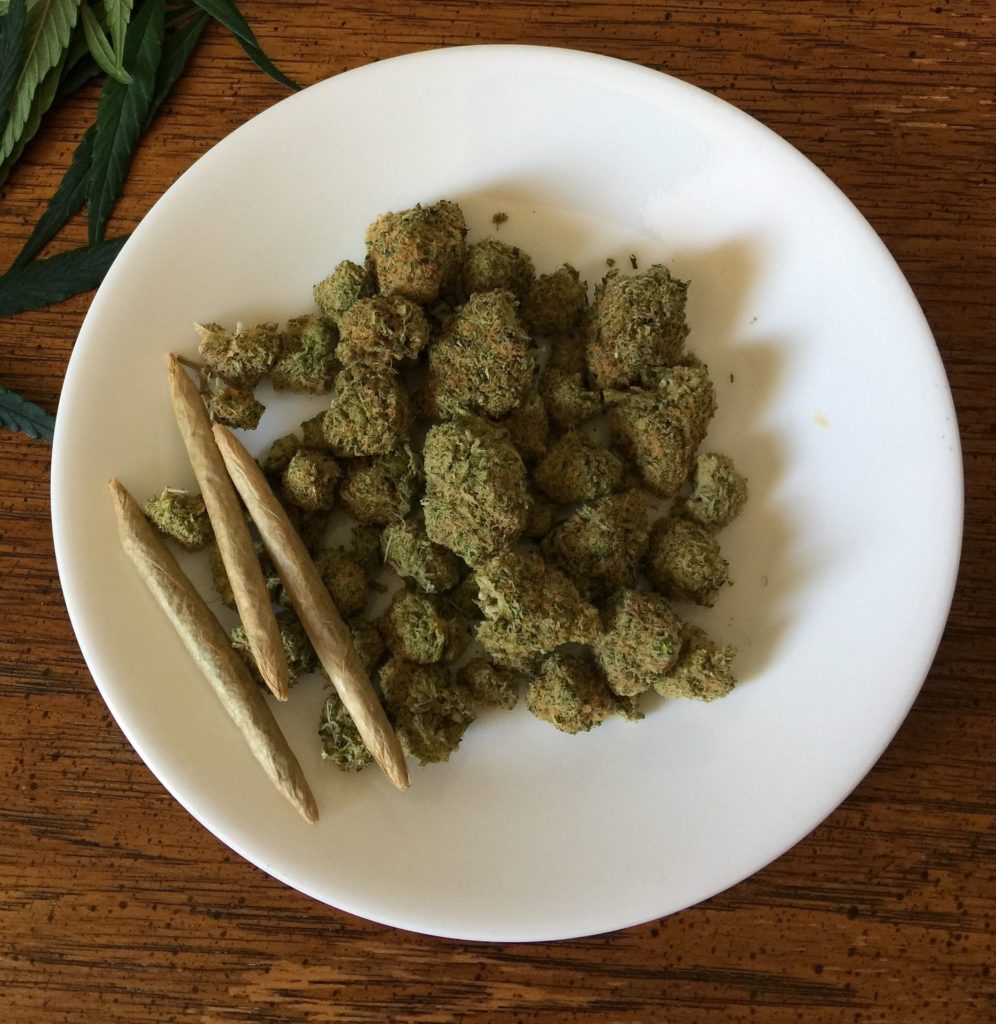 Marijuana buds and rolled joints sitting on a white plate.