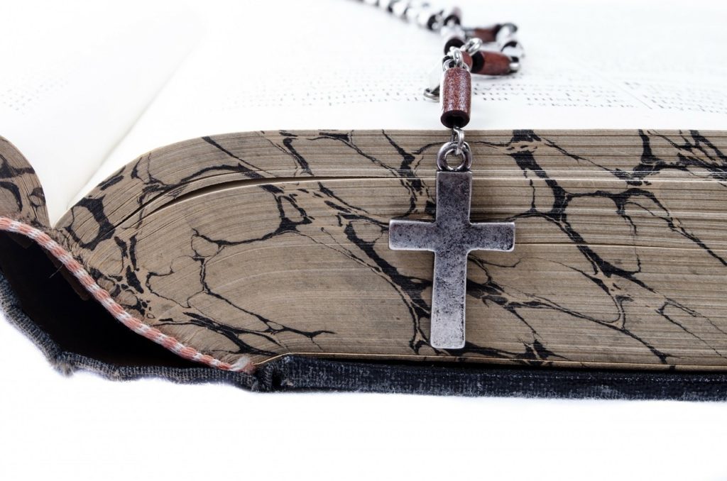 A cross on a chain sitting on an open Bible.