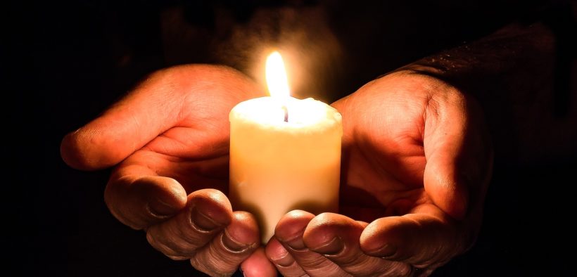 Two hands cupping a lit candle.