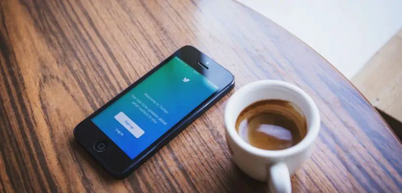 Mobile phone on a table next to a mug full of coffee.