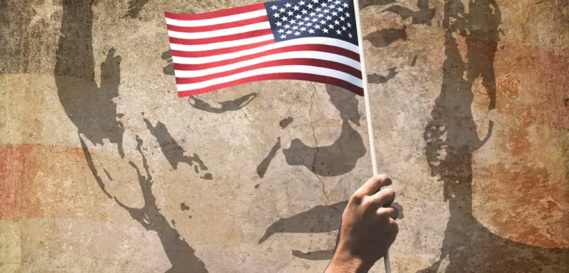 Donald Trump's face painted on a wall with a man's arm waving an American flag in front of it.