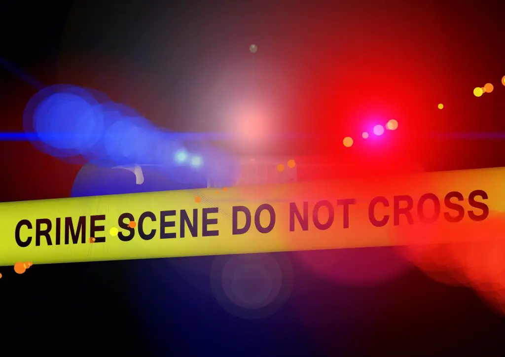 Crime scene tape with red and blue lights in the background.