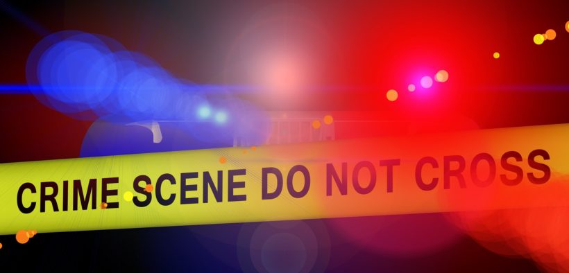 Crime scene tape with red and blue lights in the background.