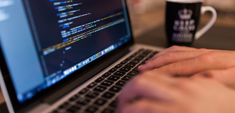 Hands typing on laptop; code appears on the screen.