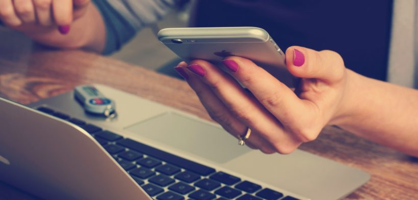 A woman holding a mobile phone over a laptop.