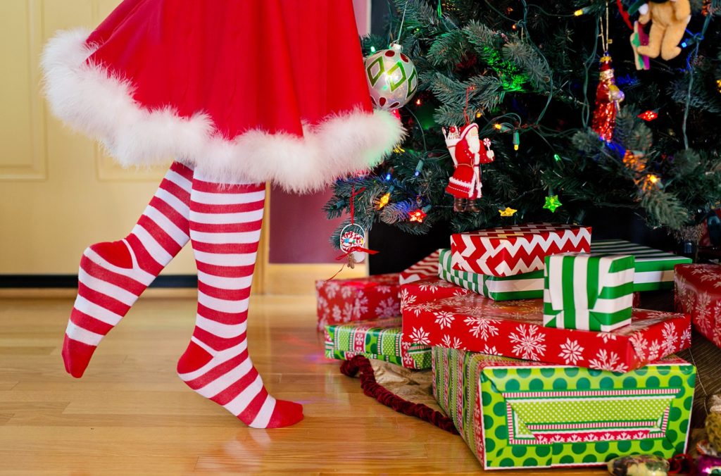 A person's legs in red and white striped socks and a white-trimmed red skirt next to a Christmas tree.