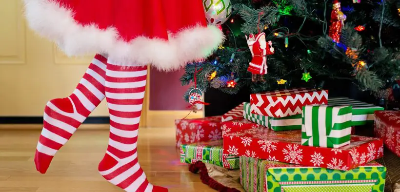 A person's legs in red and white striped socks and a white-trimmed red skirt next to a Christmas tree.