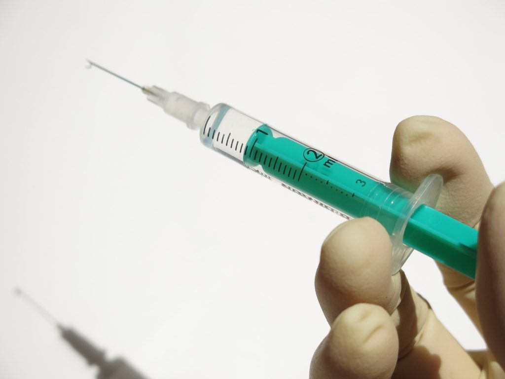 A hand in a green latex glove holding a syringe full of liquid against a white background.